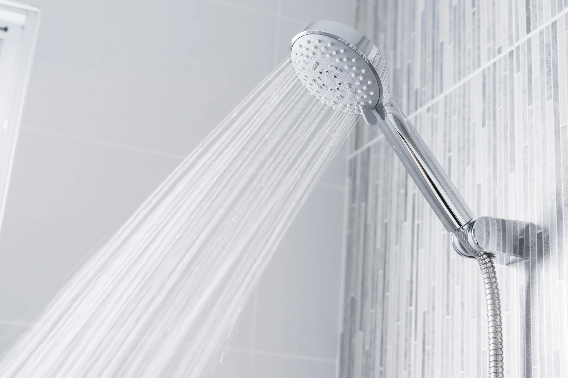 Un homme en chemise à carreaux rouge et blanc installe ou ajuste une colonne de douche dans une salle de bain carrelée blanche