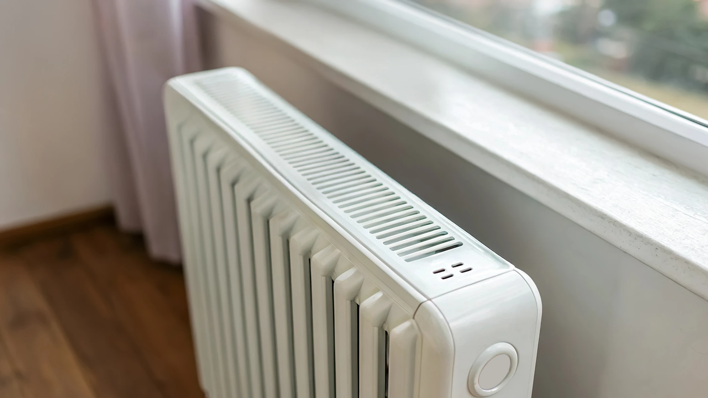 Une main ajuste le robinet thermostatique d'un radiateur à panneaux blancs dans un intérieur résidentiel aux tons chauds orangés