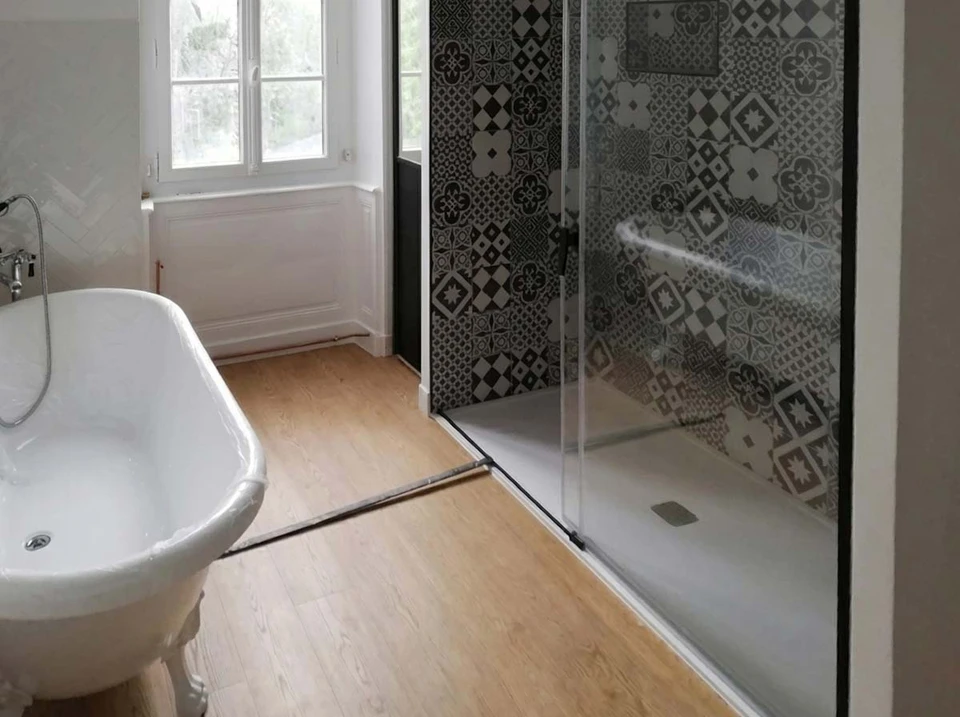 Salle de bain moderne avec double vasque intégrée en résine anthracite, meuble suspendu en bois naturel avec tiroirs et niche de rangement ouverte, robinetterie noire mate, flacons distributeurs, serviettes pliées, miroir rond avec éclairage LED, sol en terrazzo gris, mur texturé beige
