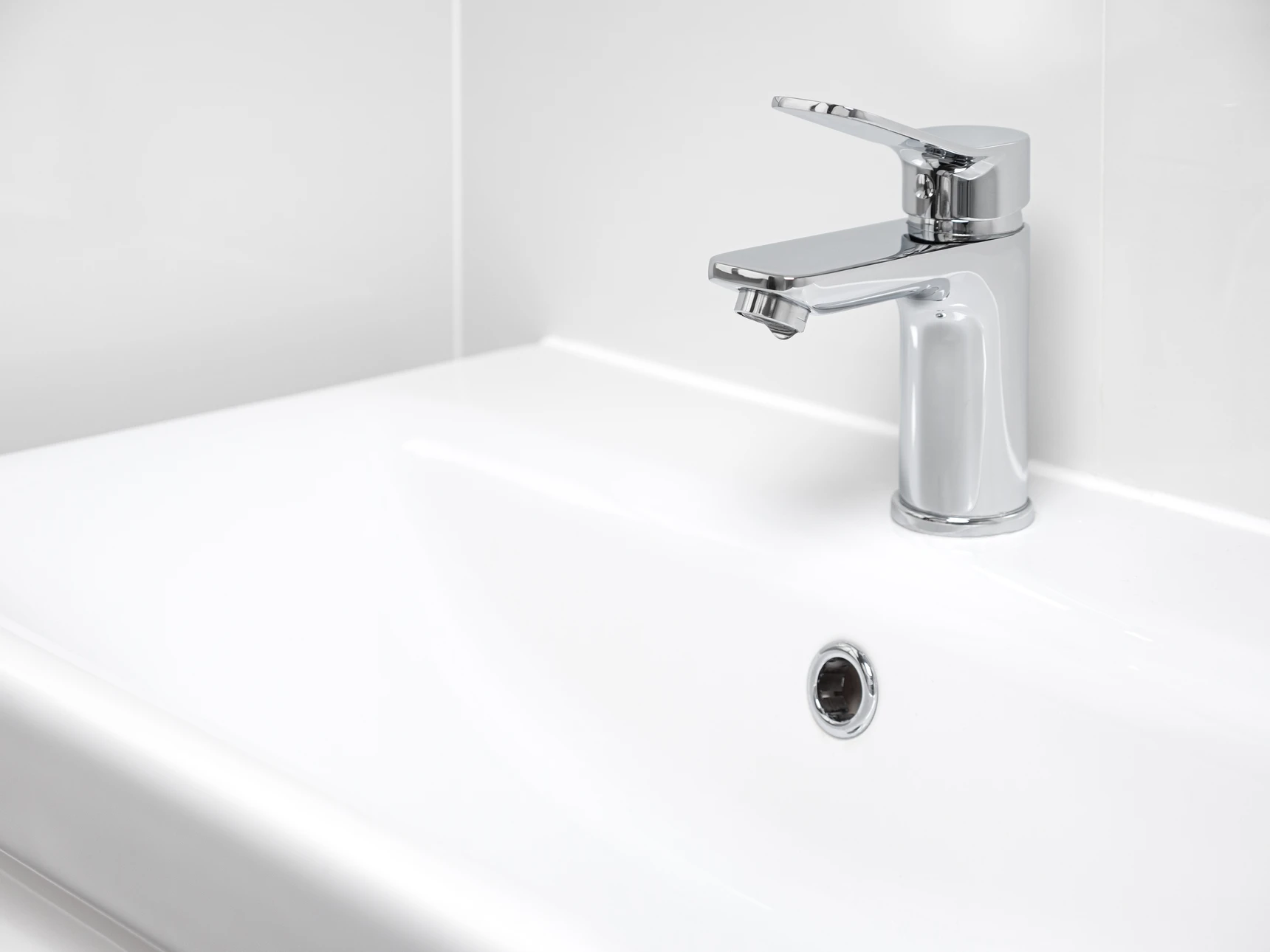 Un plombier professionnel accroupi sous un évier en cuisine ou salle de bains, détectant activement une fuite d'eau avec une lampe de poche, ou effectuant une intervention de réparation de plomberie. Contexte réel d'intérieur d'habitation, montrant la réactivité et l'expertise du professionnel dans son environnement de travail authentique.