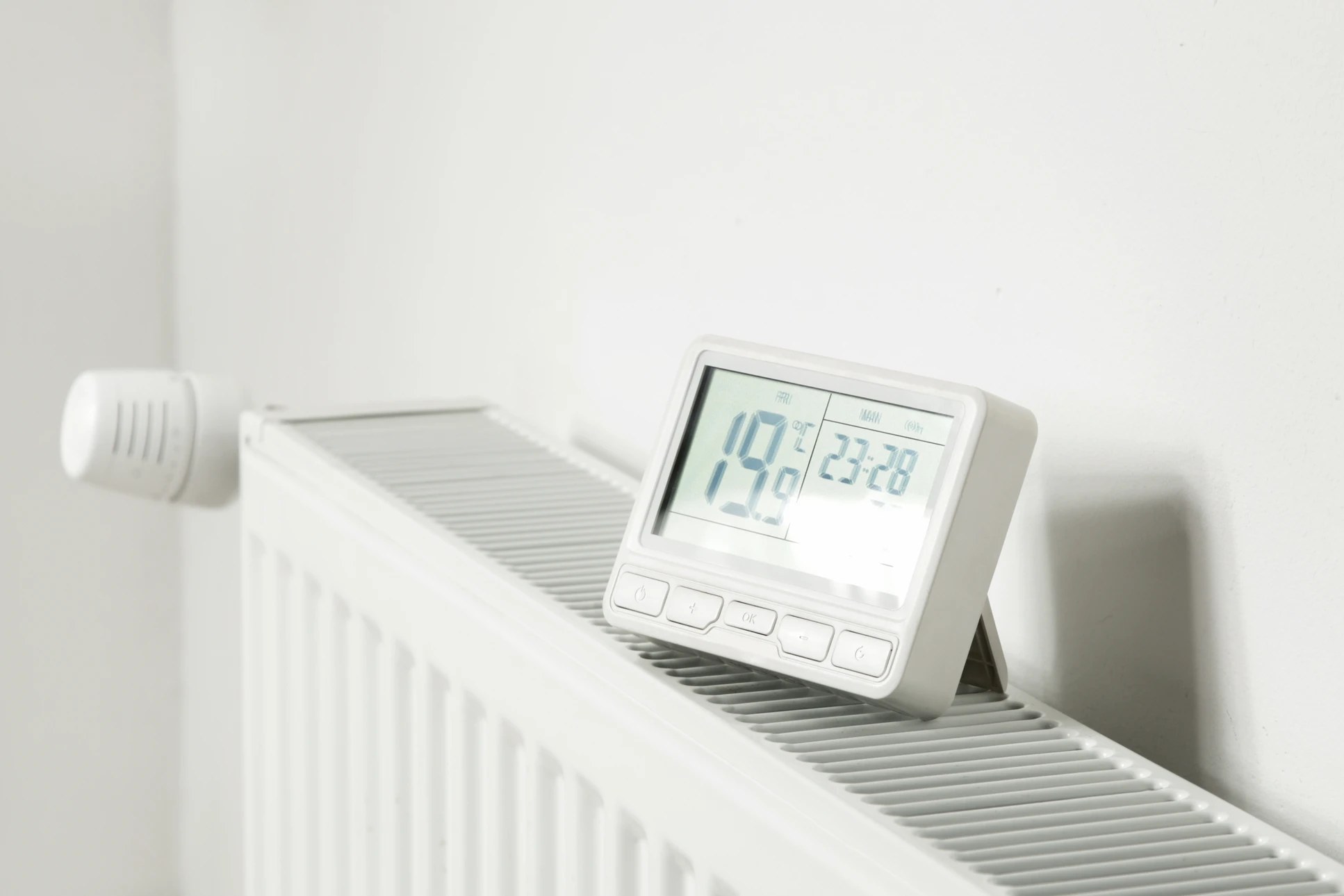 Un technicien en uniforme bleu travaille sur un radiateur mural blanc, utilisant une clé à molette pour intervenir sur la robinetterie thermostatique