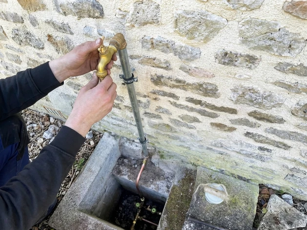Plombier en combinaison bleue effectue la réparation d'un robinet de lavabo dans une salle de bain