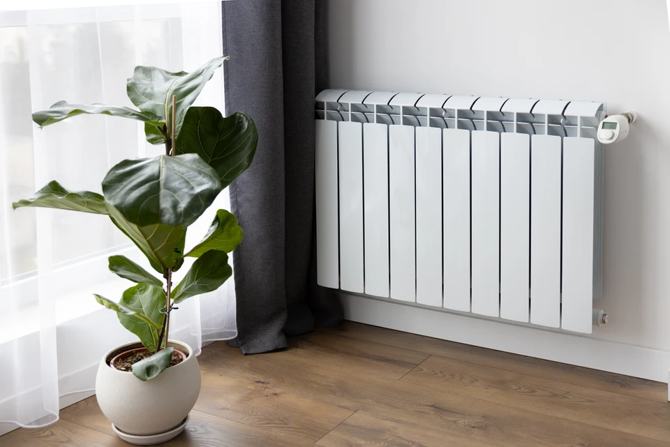 Personne en v&ecirc;tements d&eacute;contract&eacute;s contr&ocirc;lant la temp&eacute;rature d'un radiateur blanc &agrave; ailettes dans un int&eacute;rieur r&eacute;sidentiel moderne